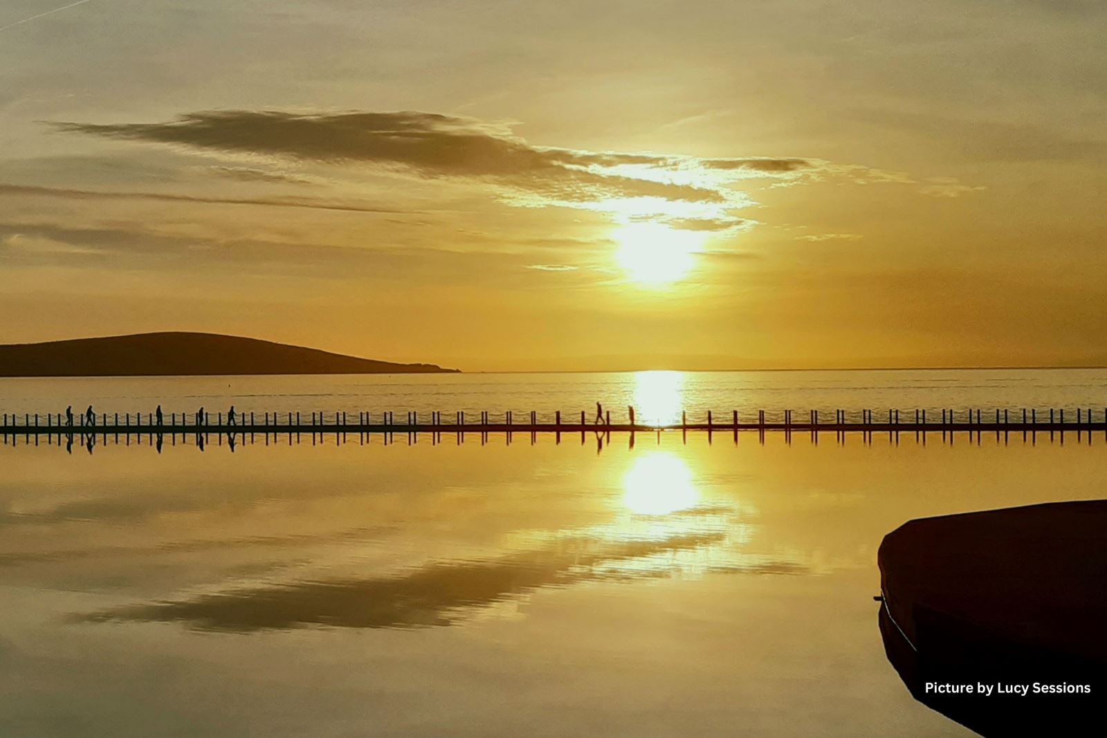 Silhouettes of people walking across the causeway at Marine Lake, Weston-super-Mare during a golden sunset